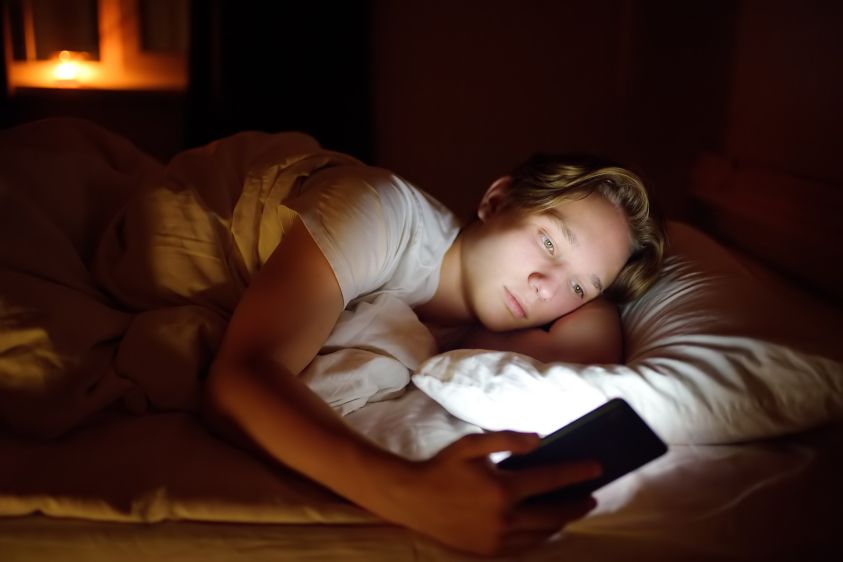 Teenager boy chatting by phone, writing in blog or reading social networks instead sleeping2e00 Young guy laying in bed and watching clips by smartphone2e00 Overuse and addiction kids from gadgets2e00